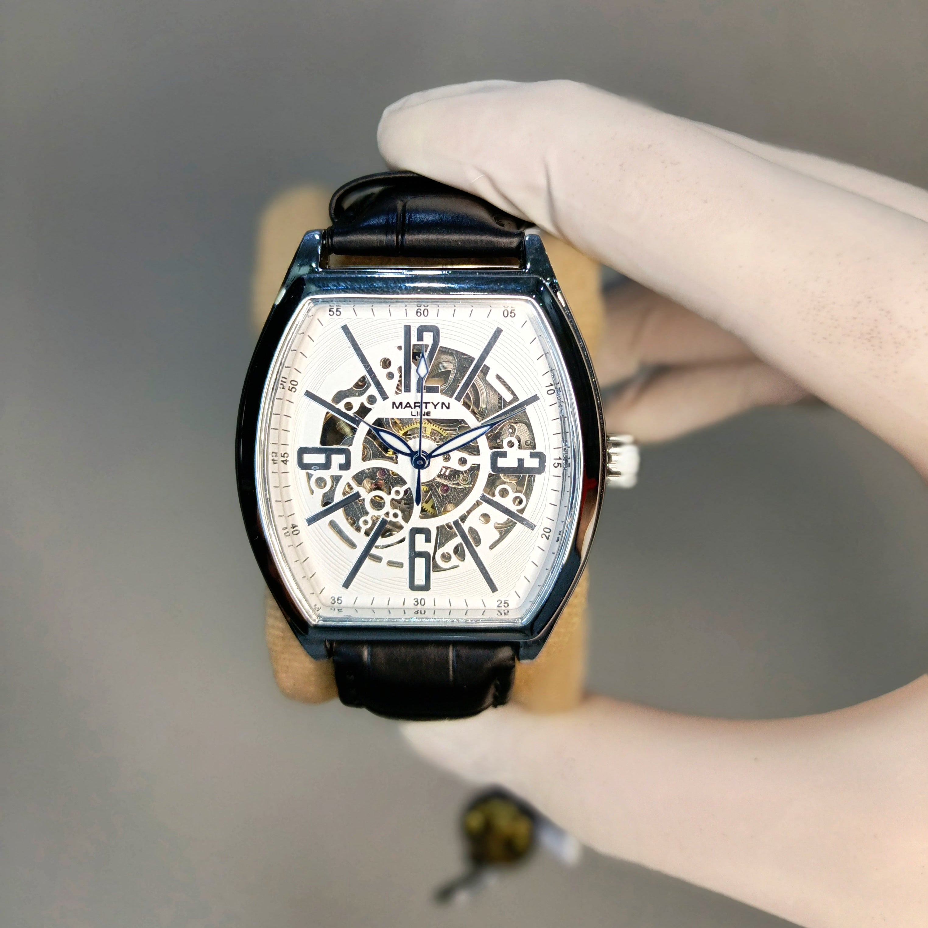 Hand holding a luxury watch with a detailed face against a neutral background