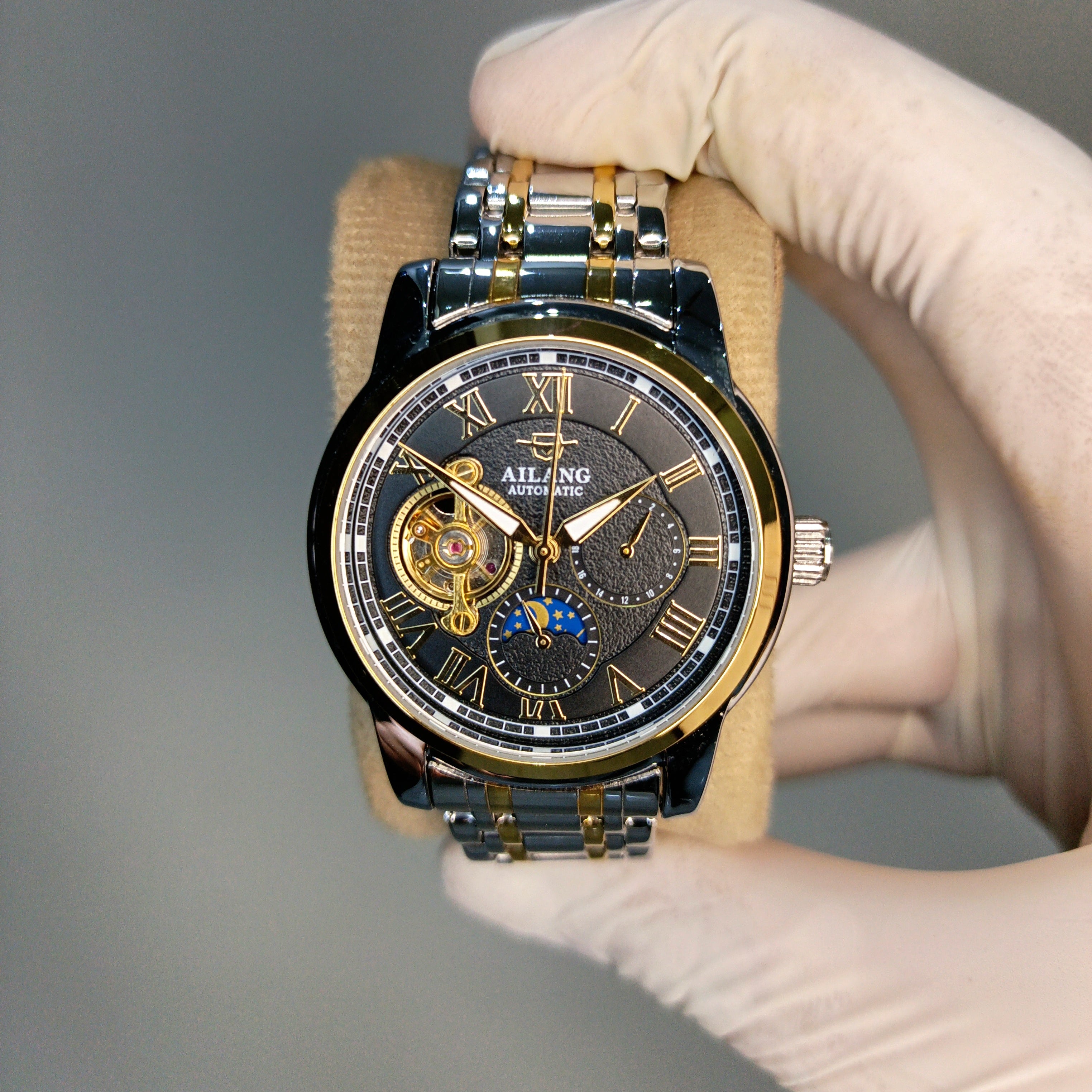 Luxury watch held by a gloved hand against a gray background