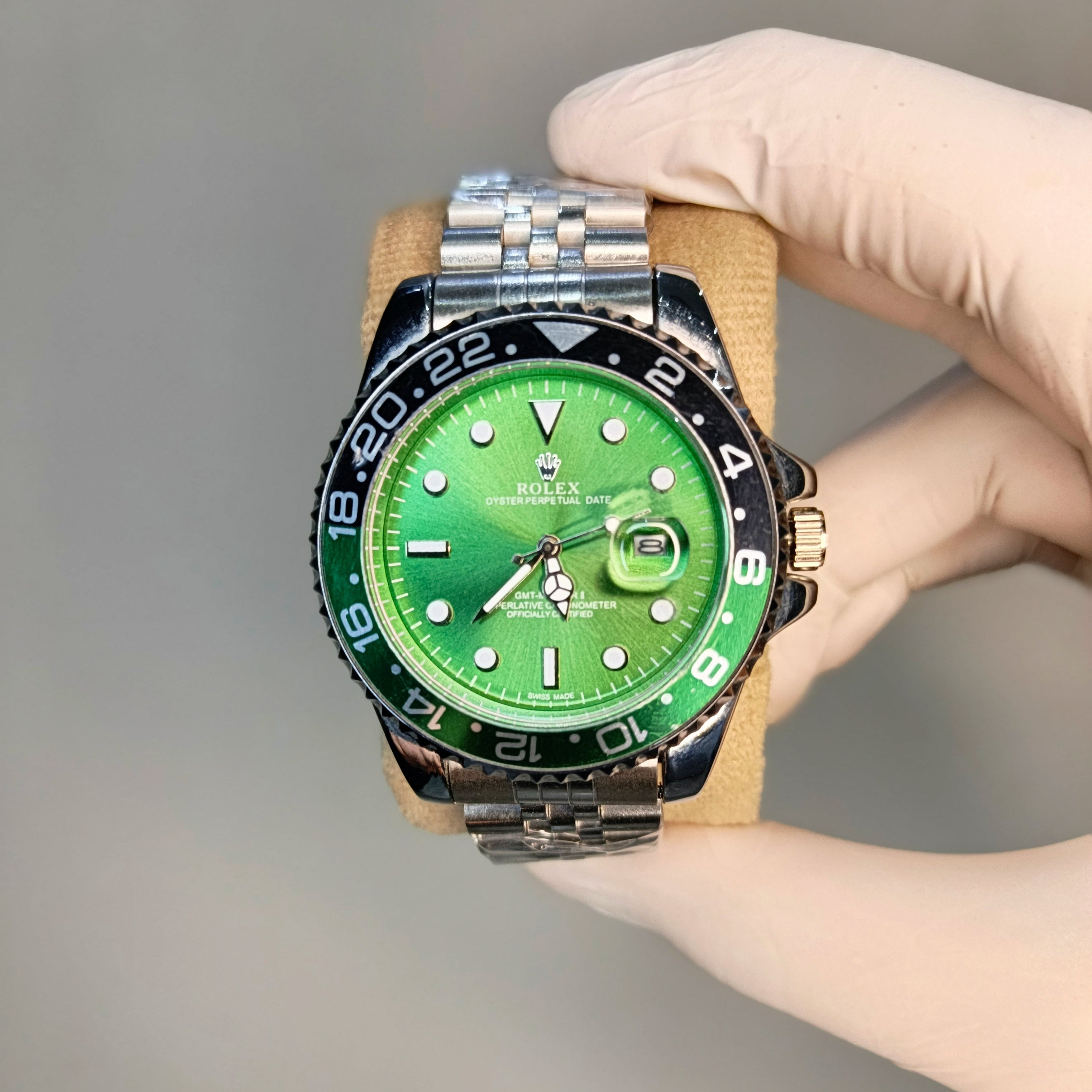 Green watch with a silver and black strap held by a gloved hand against a gray background